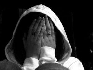 Foto in bianco e nero di ragazza con cappuccio che con le mani si copre il viso