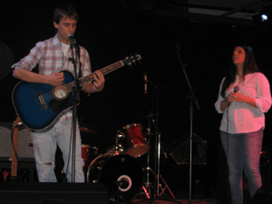 Foto di ragazzo con la chitarra e ragazza che tiene tra le mani il microfono sul palco per un'esibizione
