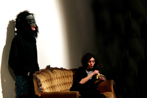 Donna su divano che mangia una banana e uomo dietro con maschera di gorilla 