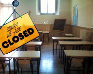 Foto di classe vuota con sopra un cartello giallo che ne comunica la chiusura