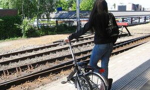Foto di ragazza che aspetta il treno con in mano una bici pieghevole