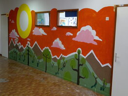 Foto di murales a colori raffigurante un bosco stilizzato realizzato su muro di edificio scolastico