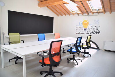 Foto interno spazio coworking con lavagna, tavolo riunioni e sedie girevoli
