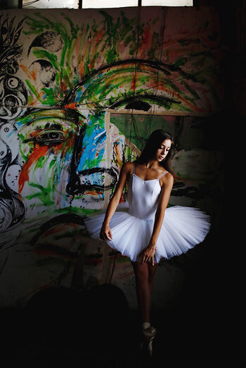 Una delicata ballerina in tutù bianco davanti ad un'opera di Carlo Gori al MAAM di Roma